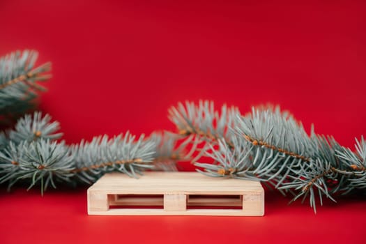 Happy New Year 2022. Wooden podium in form of pallet on red surface with Christmas tree branches. Podium, pedestal or stage. Mockup for products on red background. Merry Christmas.