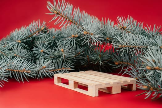 Happy New Year 2022. Wooden podium in form of pallet on red surface with Christmas tree branches. Podium, pedestal or stage. Mockup for products on red background. Merry Christmas.