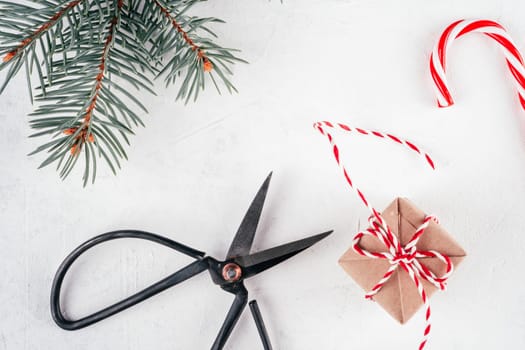 Christmas gift box and lollipop, cord, scissors on white concrete background with branch of Christmas tree. Merry Christmas and Happy New Year. Top view