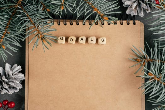 Happy New Year. Open brown kraft paper folded notebook on spring with Goals written on wooden cubes. Christmas tree branches and pine cones. Merry Christmas. Top view. Copy space