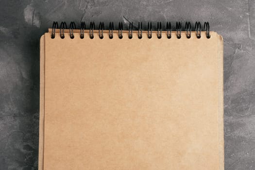 Opened brown kraft paper notebook on spring on gray concrete surface. Top view. Copy space