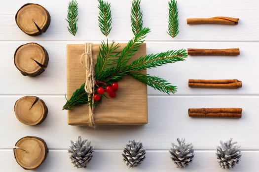 Gift with green branches of a Christmas tree, red berries, cones, cinnamon sticks on a background of white boards. Flat lay.