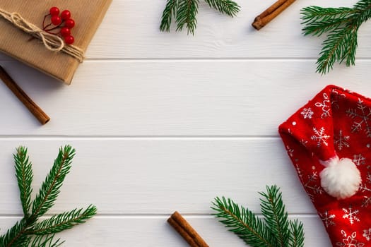Gift with green branches of a Christmas tree, red berries, cones, cinnamon sticks on a background of white boards. Flat lay. Copy space.