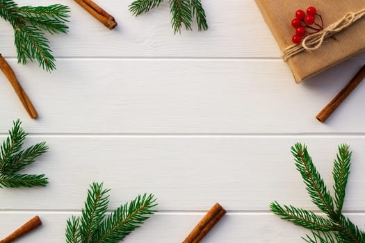 Gift with green branches of a Christmas tree, red berries, cones, cinnamon sticks on a background of white boards. Flat lay. Copy space.