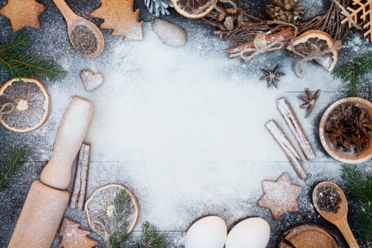 Flour New Year background. Christmas tree branches, gingerbread cookies, spices and baking supplies on black wood background. Christmas, New Year greeting card
