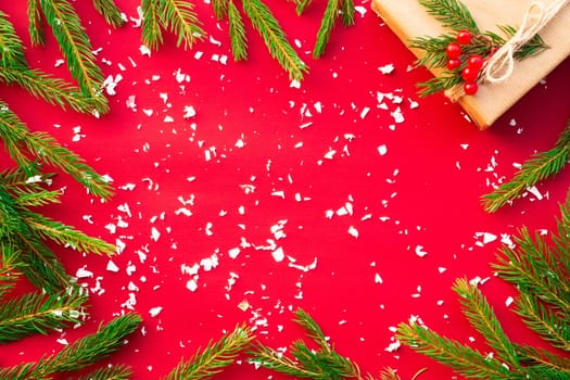 Gift wrapped in craft paper with green branches of a Christmas tree and red berries on a red background. Flat lay. Copy space.
