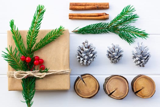 Gift with green branches of a Christmas tree, red berries, cones, cinnamon sticks on a background of white boards. Flat lay.