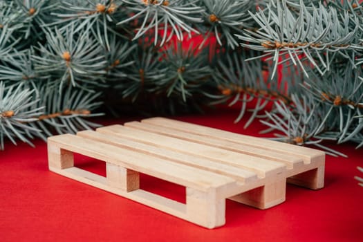 Happy New Year 2022. Wooden podium in form of pallet on red surface with Christmas tree branches. Podium, pedestal or stage. Mockup for products on red background. Merry Christmas.