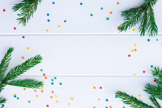 Green branches of a Christmas tree and confetti on a background of white boards. Flat lay. Copy space