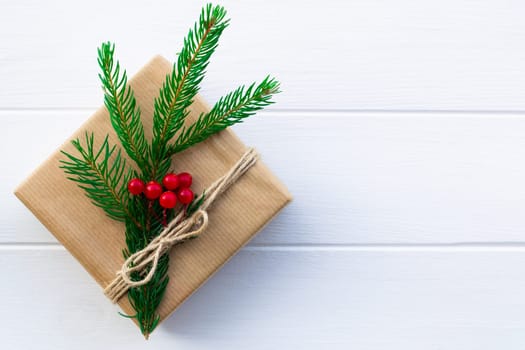 Gift with green branches of a Christmas tree and red berries on a background of white boards. Flat lay. Copy space