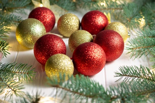 Green branches of a Christmas tree with LED light bulbs, garland and shiny balls on a white wooden background. Merry Christmas and Happy New Year concept
