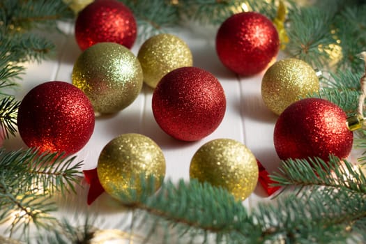 Green branches of a Christmas tree with LED light bulbs, garland and shiny balls on a white wooden background. Merry Christmas and Happy New Year concept