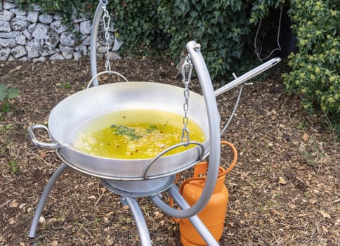 Chopped Garlic and onion frying with olive oil in a big frying pan outdoor close up. Traditional italian and apulian cousine, cooking for huge family or friends in the backyard