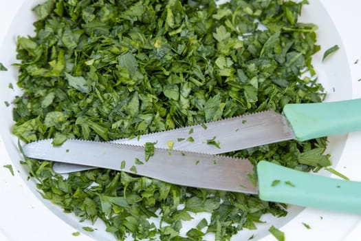 Fresh Chopped parsley on a plate with knives top view. Traditional Mediterranean cuisine. Cooking vegetarian salad for a big family..
