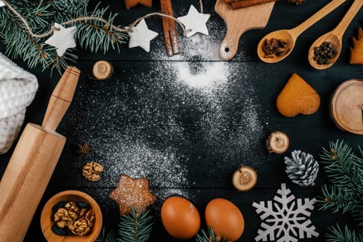 Branches of Christmas tree, gingerbread cookies, baking accessories and ingredients lying on black wooden table with sprinkled flour. Copy space. Merry Christmas and Happy New Year. Top view