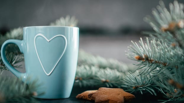 Partially blurred blue cup with heart with Christmas tree branches and gingerbread cookies. Copy space.