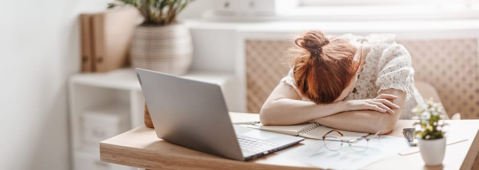 Tired woman putting her head on her hands on the desk in the office. Concept of overworked.
