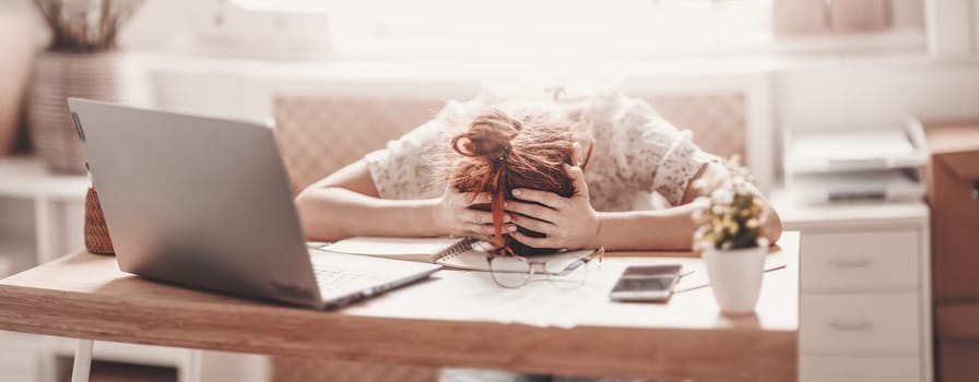 Tired woman putting her head on her hands on the desk in the office. Concept of overworked.