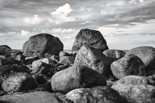 Big stones in black and white taken on stone beach in front of sea with clouds in sky. Denmark in Scandinavia. Landscape shot from nature in the north