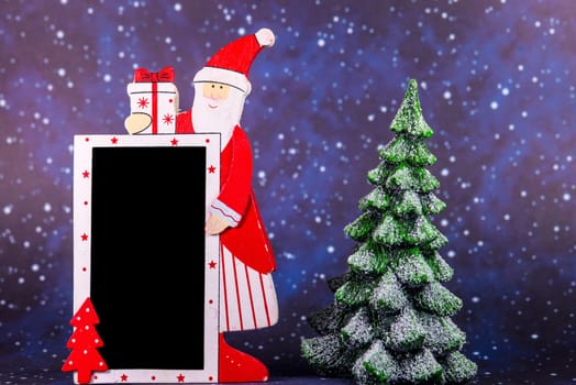 Santa Claus with empty blackboard and snowy fir tree