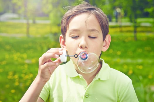 Handsome boy blowing soap bubbles in park