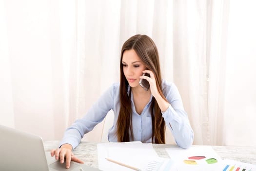 Businesswoman working at the office with the laptop and some documents and talking by the phone.