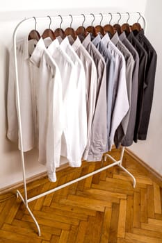 Several shirts on a hanger. from white to black color range.