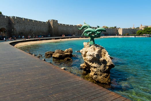 View of the dock of the pier of Rhodes with sculpture in the foreground and the city walls' in the background
