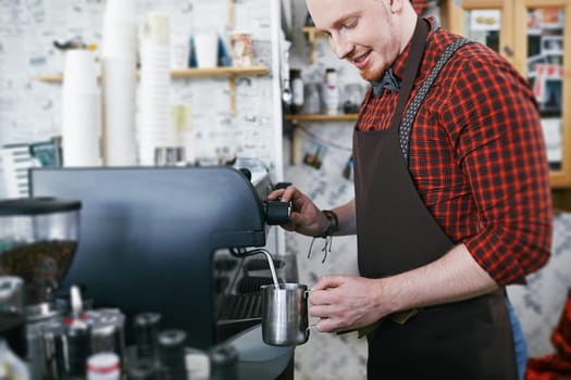 Young man in apron using coffee machine