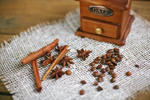Wooden coffee grinder with coffee beans, star anise and cinnamon sticks on napkin