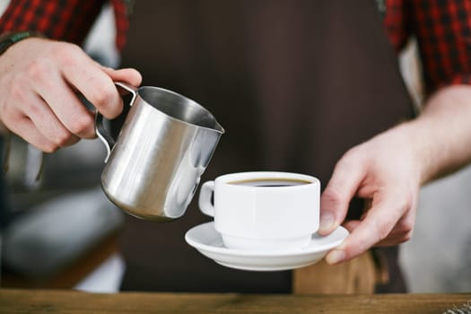 Hands of barista adding milk or water in black coffee