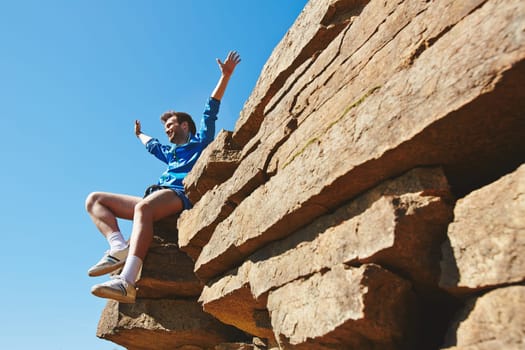 Happy man with raised arms sitting on top of rock