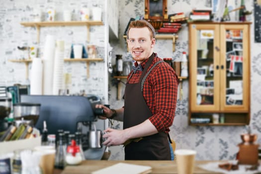 Happy man in apron looking at camera while making coffee