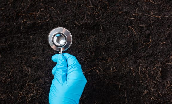 Hand of researcher woman wear gloves holding a stethoscope on fertile black soil for check condition before agriculture or planting, Concept of World Soil Day, Earth day and hands ecology environments