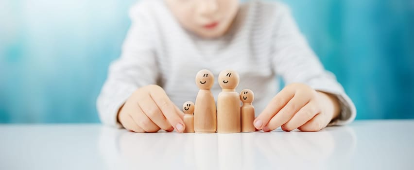 Child sitting at the table with wooden figures of the family on it. Concept of the love, safety and relation between peoples.