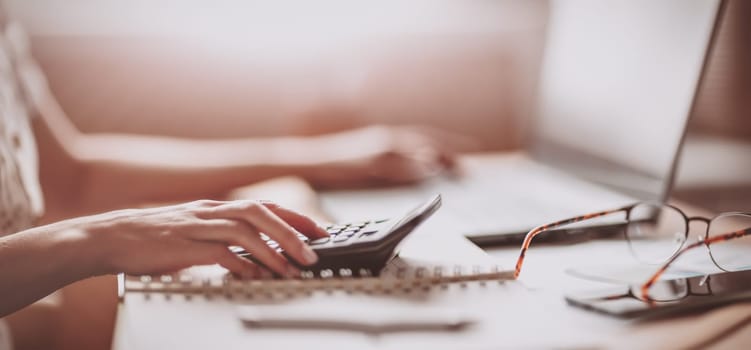 Woman working with laptop and calculator at home office. Panoramic view. Concept of the freelancer.