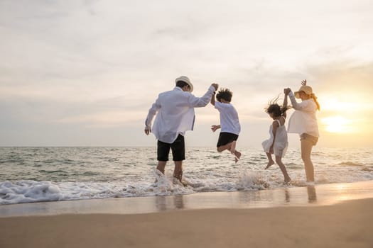 Back people enjoying travel trip and vacations, Silhouette of family father, mother, son and daughter holding hands together on beach, Happy family have fun jumping on beach in holiday at sunset