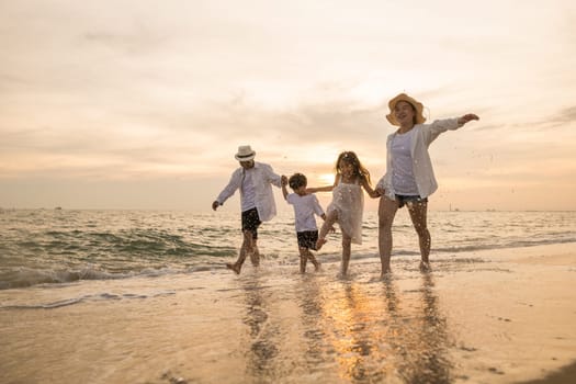 Tropical summer vacations, Happy family having fun running on a sandy beach at sunset time, People of father, mother, children son and daughter family of four holding hands together walking on beach