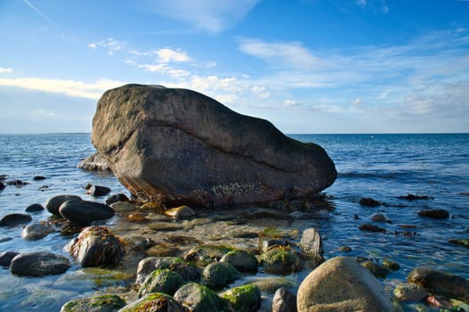Large stone in the water on the beach in the sea. Danish coast on a sunny day. Landscape shot on the water