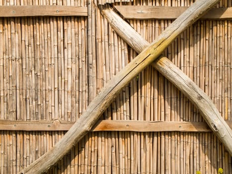 Format-filling view of a fence with vertical bamboo poles arranged close together and reinforced with softwood cross bracing..