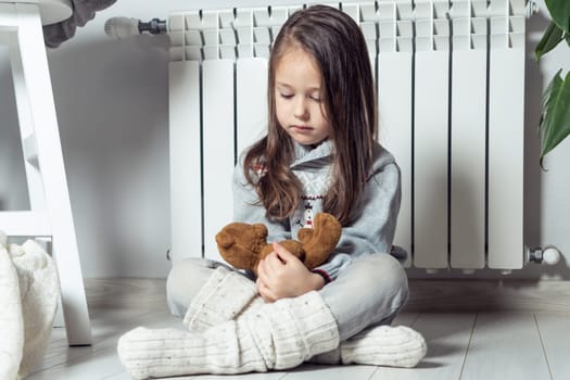 Calm, independent, nice little girl warming up near heating radiator and playing with stuffed soft bear toys and having fun on the floor, care about imaginary friends. Daycare, creative games