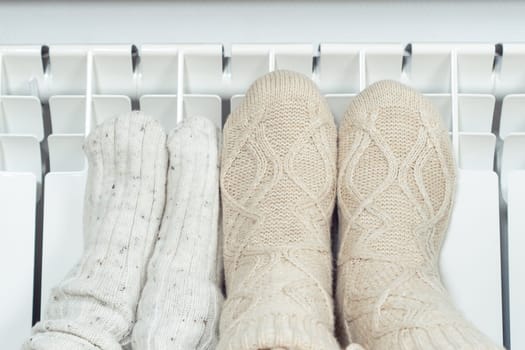 Unrecognizable cozy, cute pair child and adult frozen feet in wool, knitted socks warm themselves near gas or electric heat radiator. Central heating in cold winter season. Economic crisis and savings