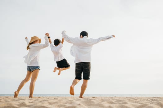 Family outdoor activities, Back family mother, father and son holding hands and jumping in air at dawn time, Happy Asian family people have fun together on beach on holiday summer vacation travel