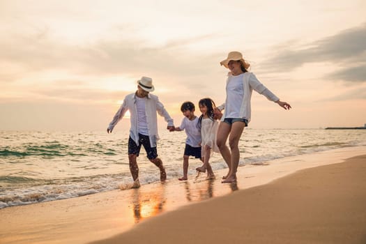 Happy family having fun running on a sandy beach at sunset time, Active parents and people father, mother, children son and daughter holding hands together walking on beach, tropical summer vacations