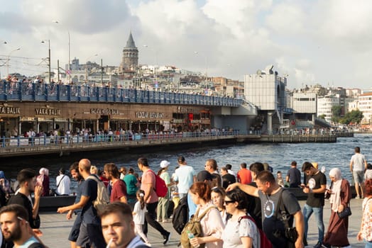 Istanbul, Turkey - August 30 2022: Eminonu Square overlooking Galata Bridge with traditional fish restaurants in the passage under the bridge, Galata Tower, and crowds of People during Victory Day