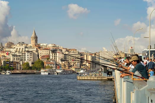 Istanbul, Turkey - August 30, 2022: Local citizens fishing at Golden Horn on Galata Bridge before sunset with Skyline of Istanbul in the background, including Galata Tower, at Eminonu district