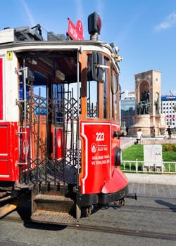 Istanbul, Turkey - September 2 2022: Nostalgic Taksim Tunel Red Tram, or tramvay, with Republic Monument, or Cumhuriyet Aniti Statue in the background, at Taksim Square, Beyoglu district, city center