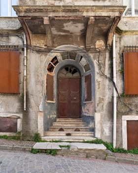 Exterior shot of grungy abandoned entrance with rusted metal door, and stairs, on a cobblestone narrow street