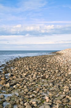 Stone beach by the sea. Danish coast on a sunny day with clouds in the sky. Landscape shot at the water