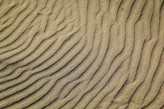 A texture of sand on the beach created by wind and waves.